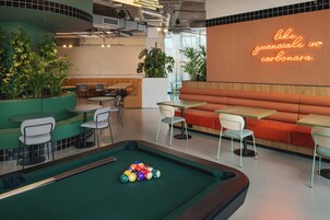 A pool table with balls, a billiards area, seating with tables and chairs, and a neon sign.