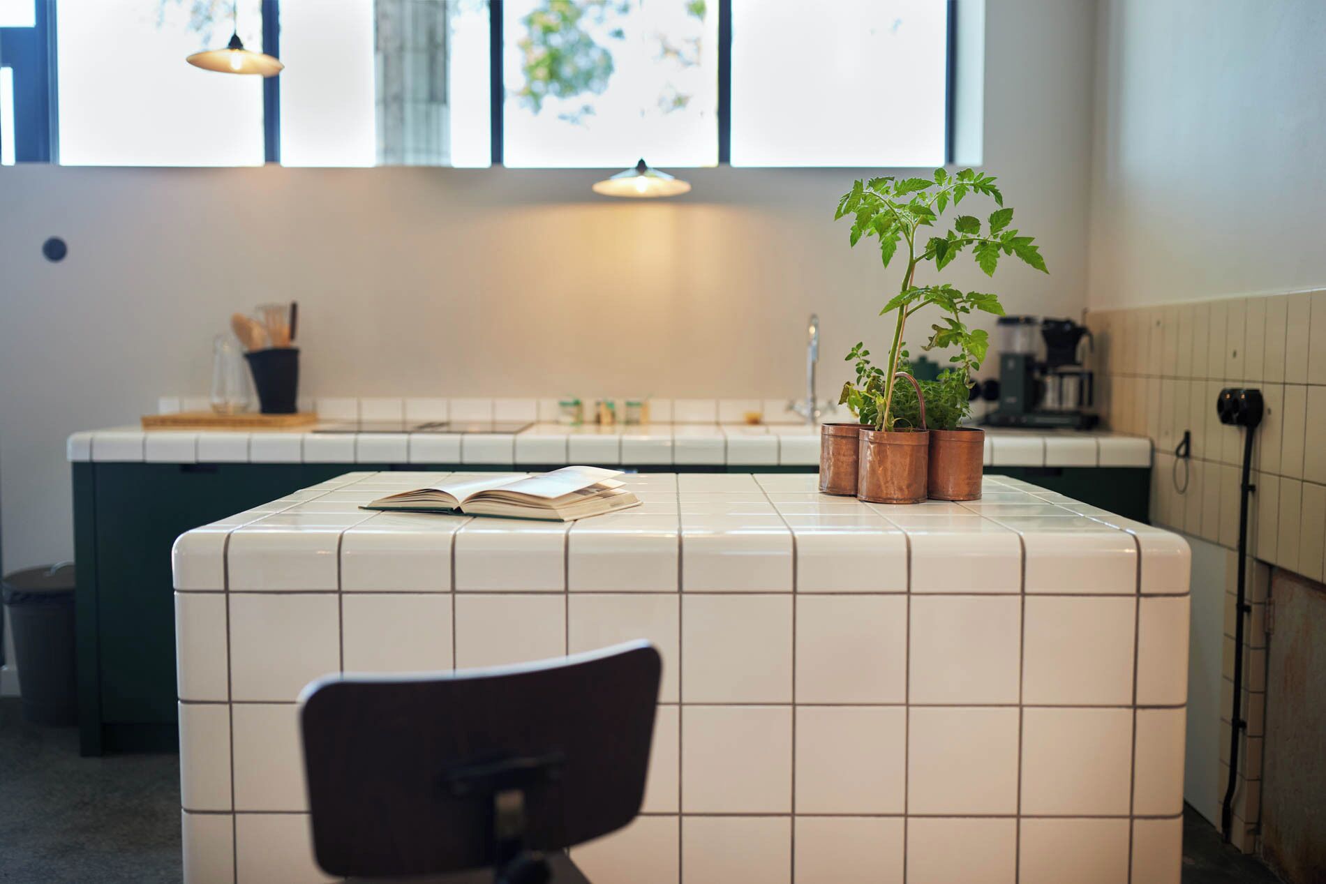 A kitchen with white tiles, a countertop with a plant, and a chair.