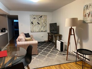 A modern living room with a sofa, a glass table, a TV, a lamp, and a painting on the wall.
