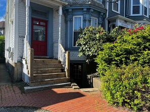 A two-story house with a red front door, a brick pathway, and a garden with green shrubs.