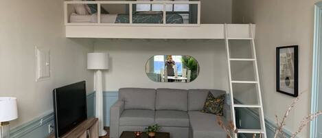 A loft-style room with a sofa, a television, a small table, a lamp, and a ladder.