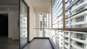A balcony with a view of other buildings, a glass door, and a wooden floor. - Lux Suites Platinum Oak Residency (Nairobi)