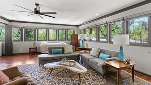Un salón amplio con ventilador de techo, ventanas grandes, sofá, mesa de centro y lámpara.