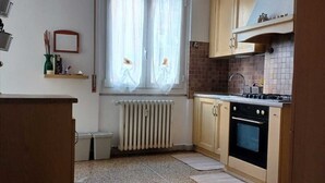 A kitchen with a radiator, wooden cabinets, a stove, and a window with curtains. - Family & Pet Friendly - 5 Seats - Near Ferry and Cruise Terminal - Port (Genova)