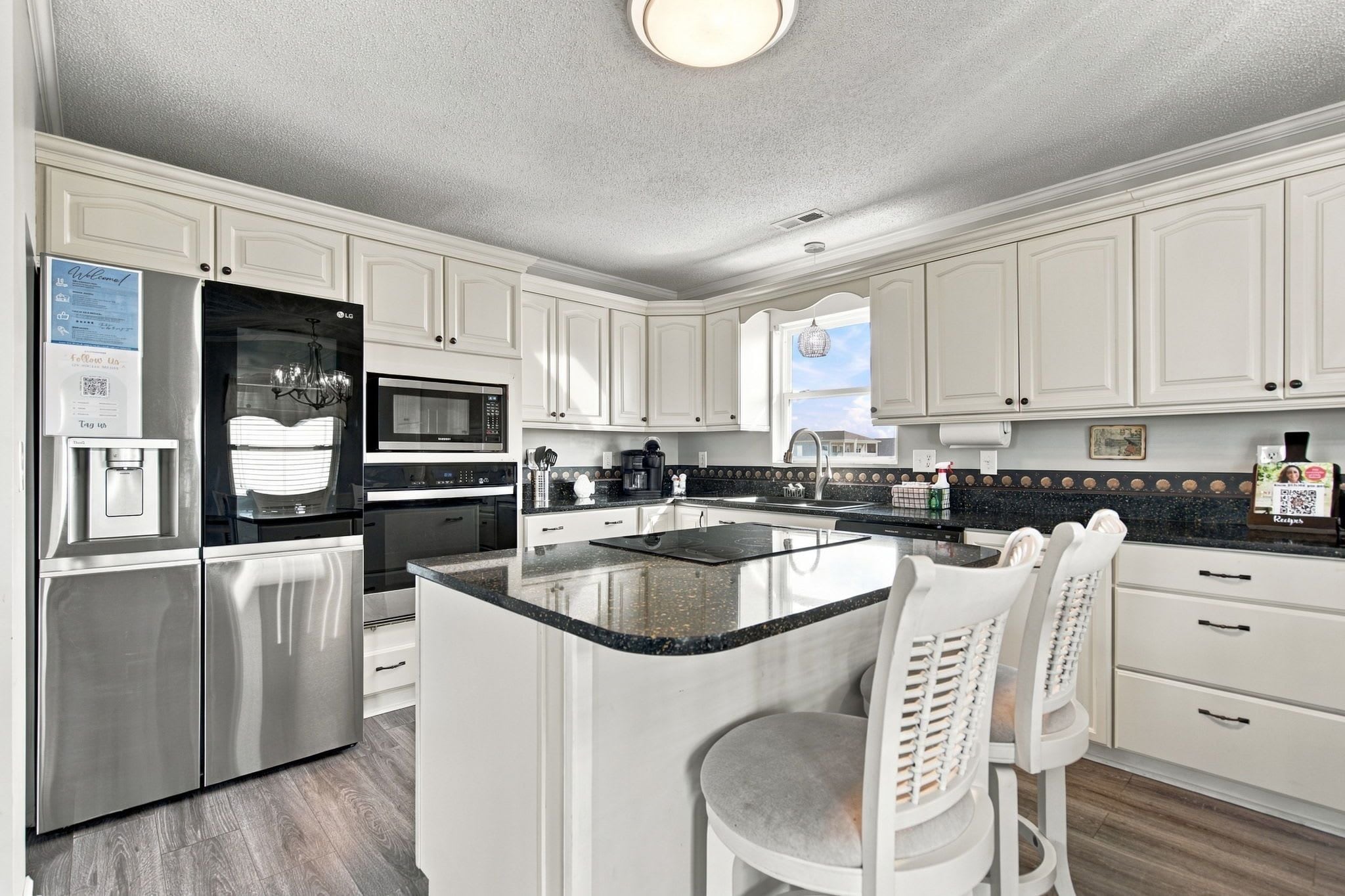 A modern kitchen with white cabinetry, stainless steel appliances, and a central island with bar stools.