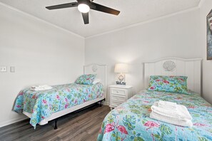 Une chambre avec deux lits, un ventilateur de plafond, une table de chevet avec une lampe et un ventilateur fixé au mur.
