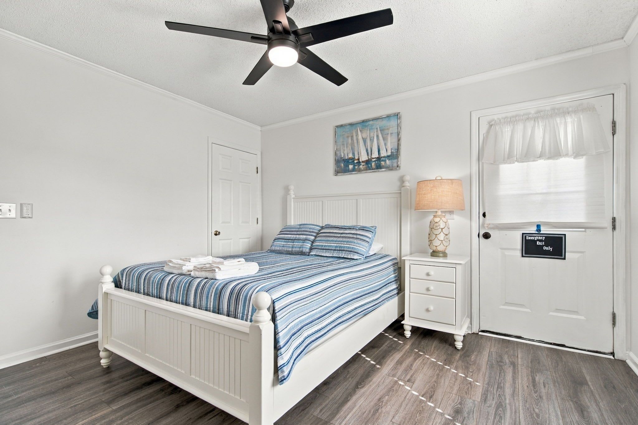 Un dormitorio con cama, mesita de noche, ventilador de techo y señal de salida de emergencia.