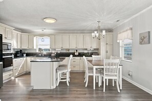 A spacious kitchen with white cabinetry, a central island, and a dining area with white chairs.