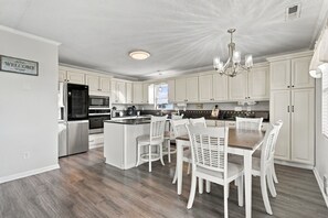 A modern kitchen with white cabinetry, a central island, and a dining area with white chairs.