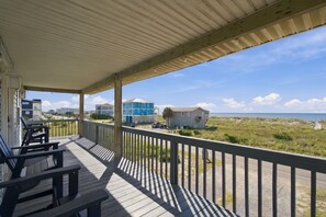 A wooden deck with a railing, overlooking a beach with houses and a clear sky.