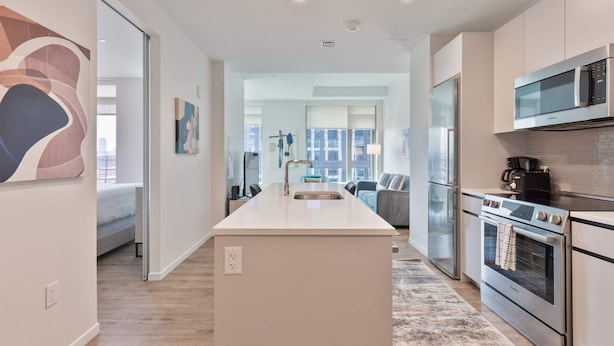 A modern kitchen with a central island, stainless steel appliances, and a view to a living area.