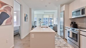 A modern kitchen with a central island, stainless steel appliances, and a view to a living area. - Luxury Apt Downtown Seaport (Boston)