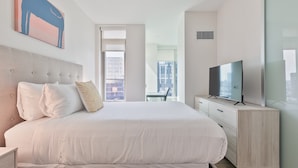 A modern hotel room with a large bed, a television, and a city view.