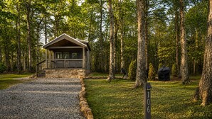 A cabin with a stone foundation and a wooden roof, surrounded by a forest. - The Ascent at The Retreat at Deer Lick Falls II (Monteagle)