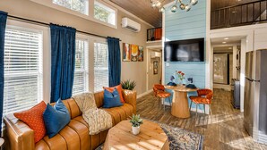 A modern living room with a brown leather sofa, a round wooden coffee table, and a dining area with orange chairs. - The Ascent at The Retreat at Deer Lick Falls II (Monteagle)