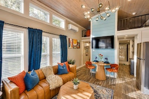 A modern living room with a brown leather sofa, a round wooden coffee table, and a dining area with orange chairs. - The Ascent at The Retreat at Deer Lick Falls II (Monteagle)