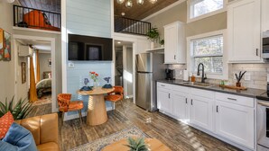 A modern kitchen with white cabinets, a stainless steel refrigerator, and a dining area with a round table and orange chairs. - The Ascent at The Retreat at Deer Lick Falls II (Monteagle)