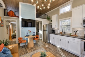 A modern kitchen with white cabinets, a stainless steel refrigerator, and a dining area with a round table and orange chairs. - The Ascent at The Retreat at Deer Lick Falls II (Monteagle)