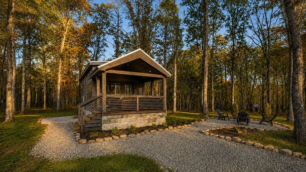 A cabin with a stone foundation, wooden exterior, and a porch with a railing. - The Ascent at The Retreat at Deer Lick Falls II (Monteagle)