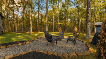 A patio with outdoor furniture, surrounded by a gravel area and a stone border, set in a wooded area.
