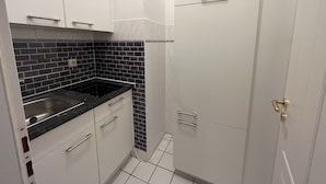 Una cocina compacta con armarios blancos, salpicadero de azulejos negros y pileta de acero inoxidable.