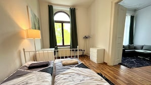 Un dormitorio con cama, escritorio, silla, radiador, armario y vistas al exterior.