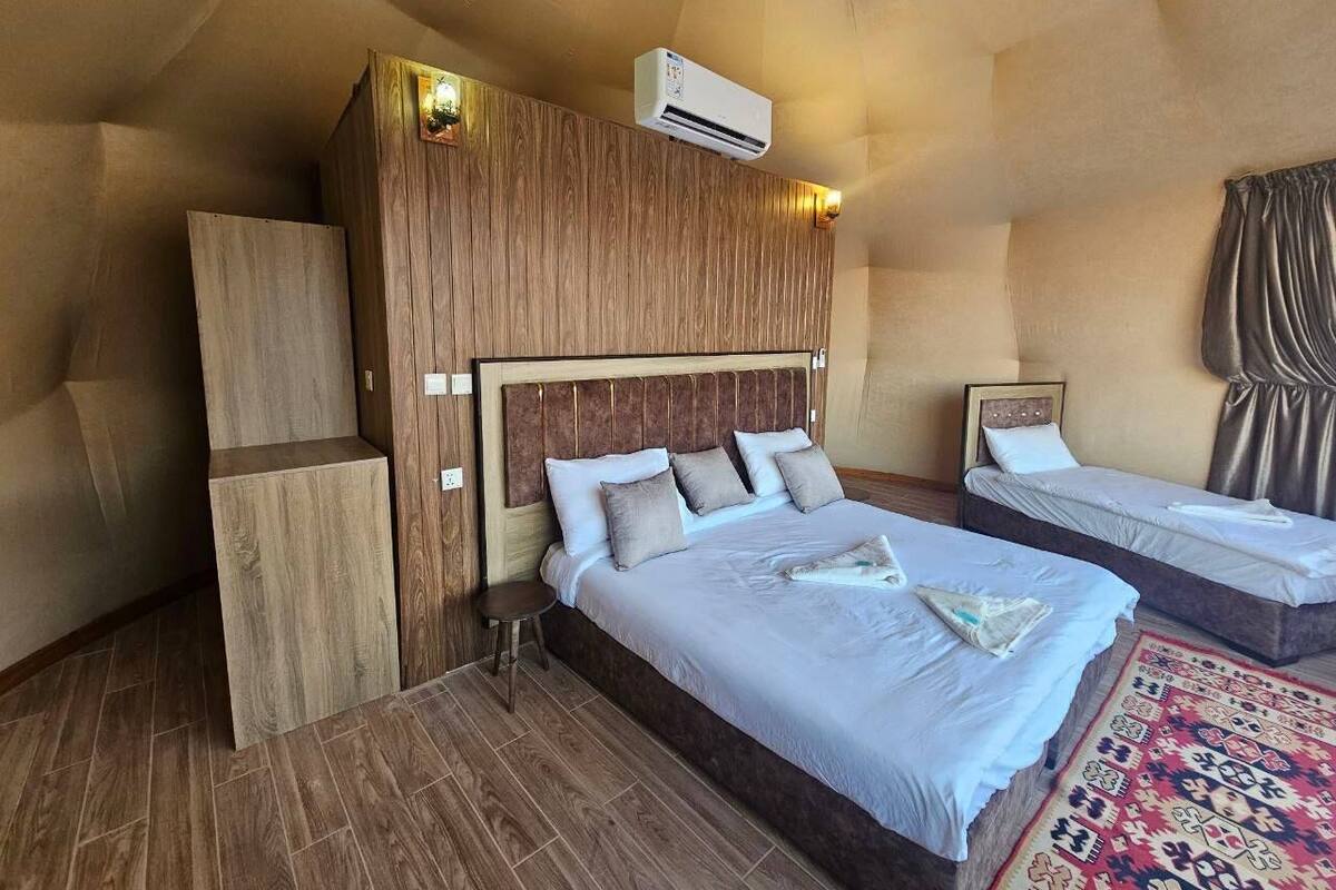 A bedroom with a large bed, a smaller bed, a wooden headboard, a nightstand, and a patterned rug.