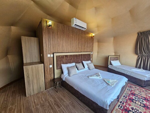 A bedroom with a large bed, a smaller bed, a wooden headboard, a nightstand, and a patterned rug. - Wadi Rum Camping (Wadi Rum)