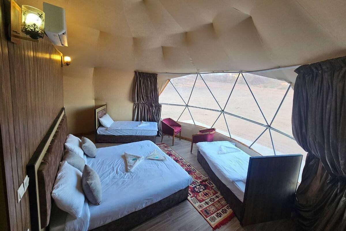 A spacious room with two beds, a small table, and a view through a large window.