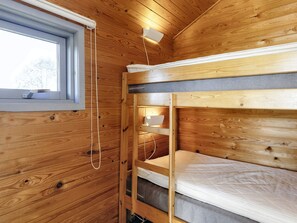 En stuga med träpanel, våningssängar, ett fönster och en liten hylla.
