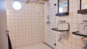 Un baño con paredes de azulejos blancos, una lámpara de techo redonda, una ducha y dos lavamanos con encimeras negras.