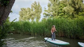 A person paddleboarding on a calm river surrounded by lush greenery and trees.