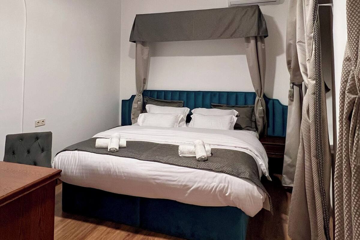 Un dormitorio con cama, escritorio, silla, lámpara en el techo y aire acondicionado de pared.