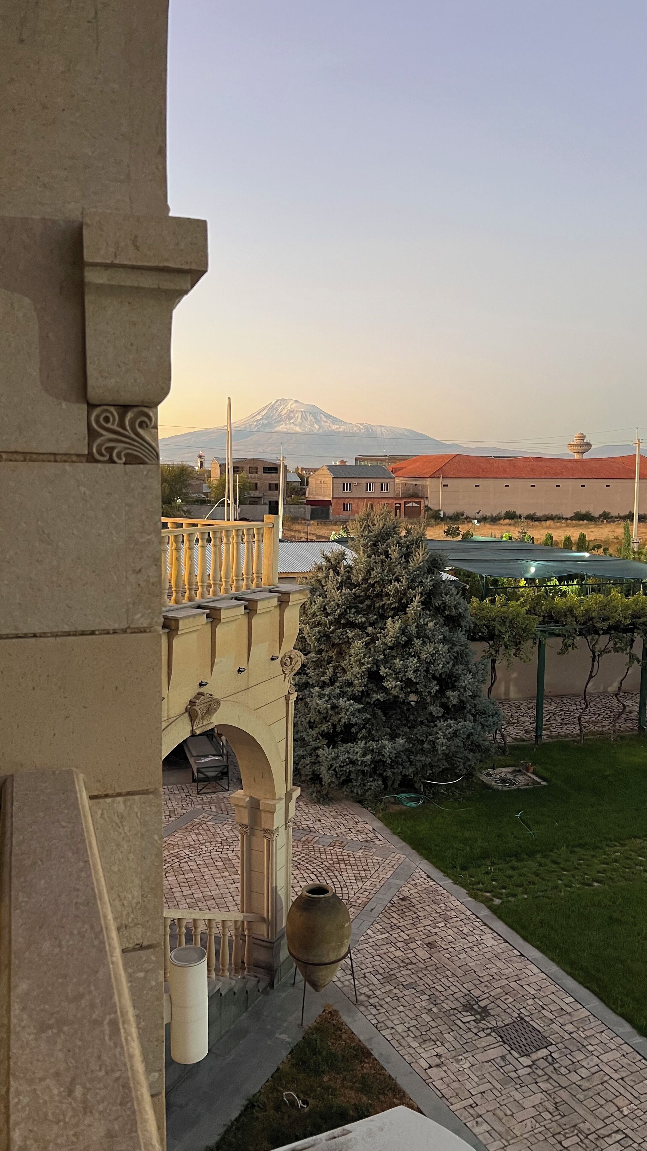 A courtyard with a view of a mountain, a pergola with vines, and a tiled walkway.