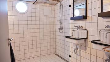 Une salle de bain avec des murs recouverts de carreaux blancs, un luminaire rond au plafond, une douche et deux vasques dotées de plans de toilette noirs.