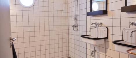 A bathroom with white tiled walls, a round ceiling light, a shower, and two sinks with black countertops.