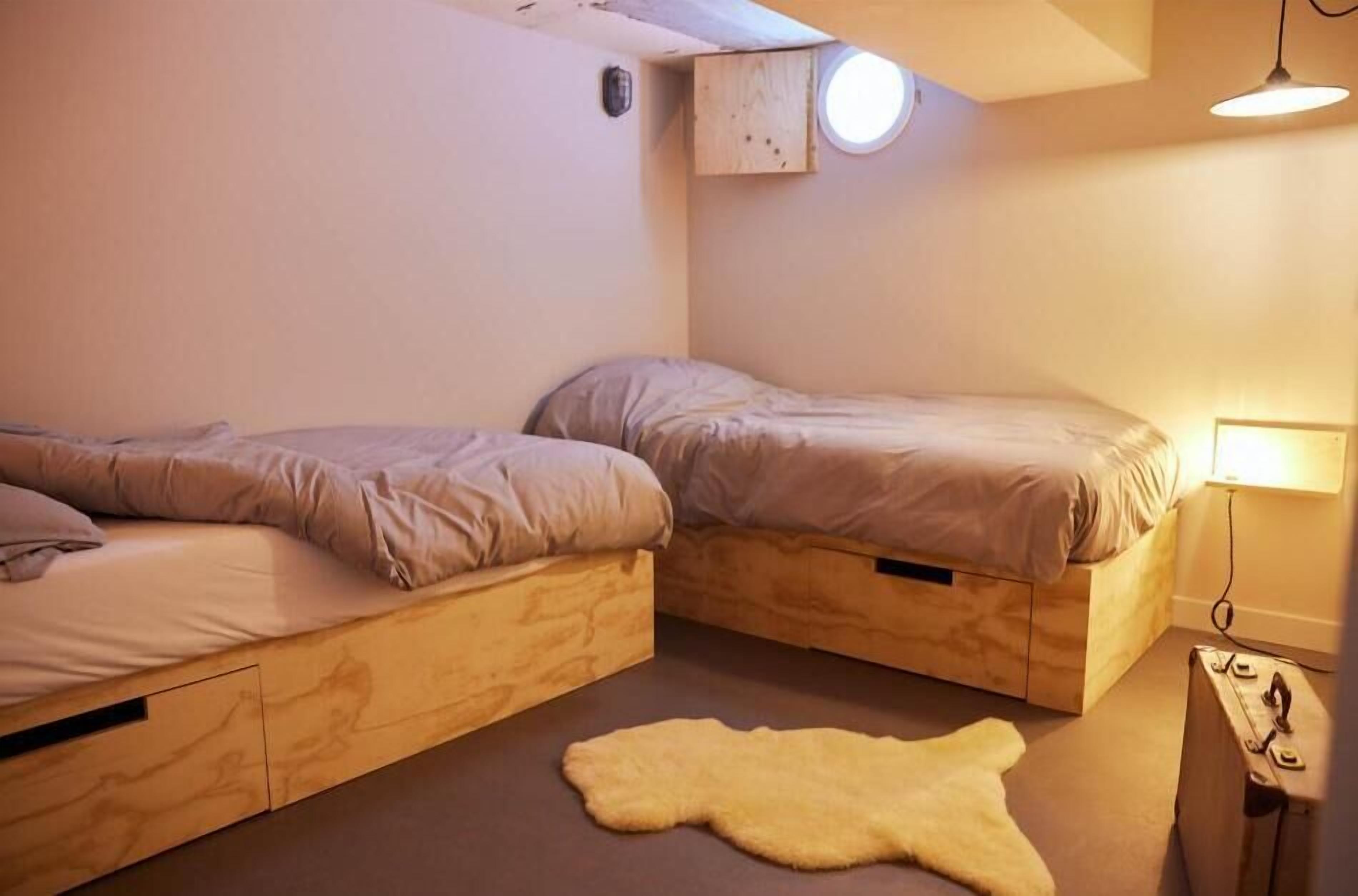 A small, cozy room with two wooden bunk beds, a round skylight, a small rug, and a lamp.