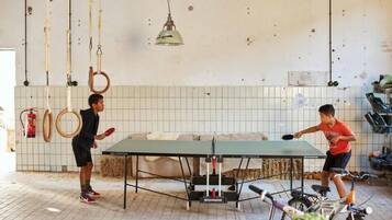 Twee personen spelen pingpong in een ruimte met een tafeltennistafel, fitnessapparatuur en een fiets.