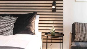 Una habitación de hotel moderna con una cama, una mesita de noche con un jarrón de flores, una silla y una lámpara de pared.
