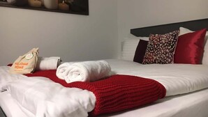 A neatly made bed with white linens, a red blanket, and a towel. A welcome bag is placed on the bed. - Apartment with shower - washing machine - 180 degree lake view (Rorschach)