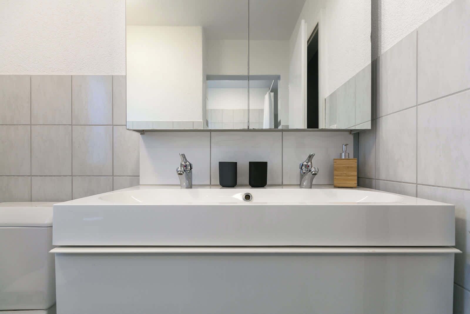 A modern bathroom with a large white sink, two faucets, and a mirror above.