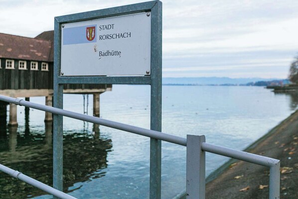 A sign with 'STADT RORSCHACH' and 'Badhütte' indicating a location by a calm river with a wooden structure in the background. - Apartment with breathtaking panoramic views (Rorschach)