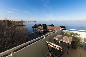 A balcony with a view of a lake, a wooden table, and a potted plant. - Apartment with breathtaking panoramic views (Rorschach)