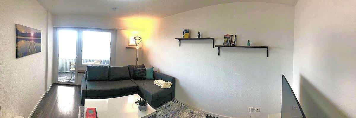 A living room with a sofa, a coffee table, a TV, and a balcony with a view.