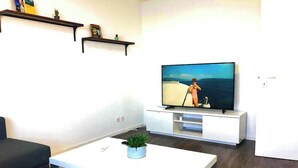 En moderne stue med et fladskærms-tv, hvide møbler og et blåt tæppe.