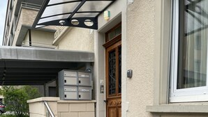 A building entrance with a set of concrete steps leading to a door, a metal handrail, and a covered outdoor area with a table and chairs.