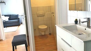 A bathroom with a toilet, sink, and mirror. There is a small stool and a potted plant.