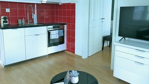 A compact kitchen with white cabinets, a red tiled backsplash, a stove, and a black countertop.