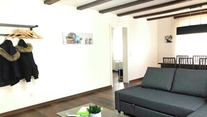 Ein Wohnzimmer mit einer Couch, einem Glastisch, einem Kleiderständer mit Mänteln und einem an der Wand befestigten Schild.