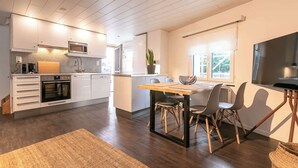 A modern kitchen with a dining area, wooden flooring, and a view of the outdoors.